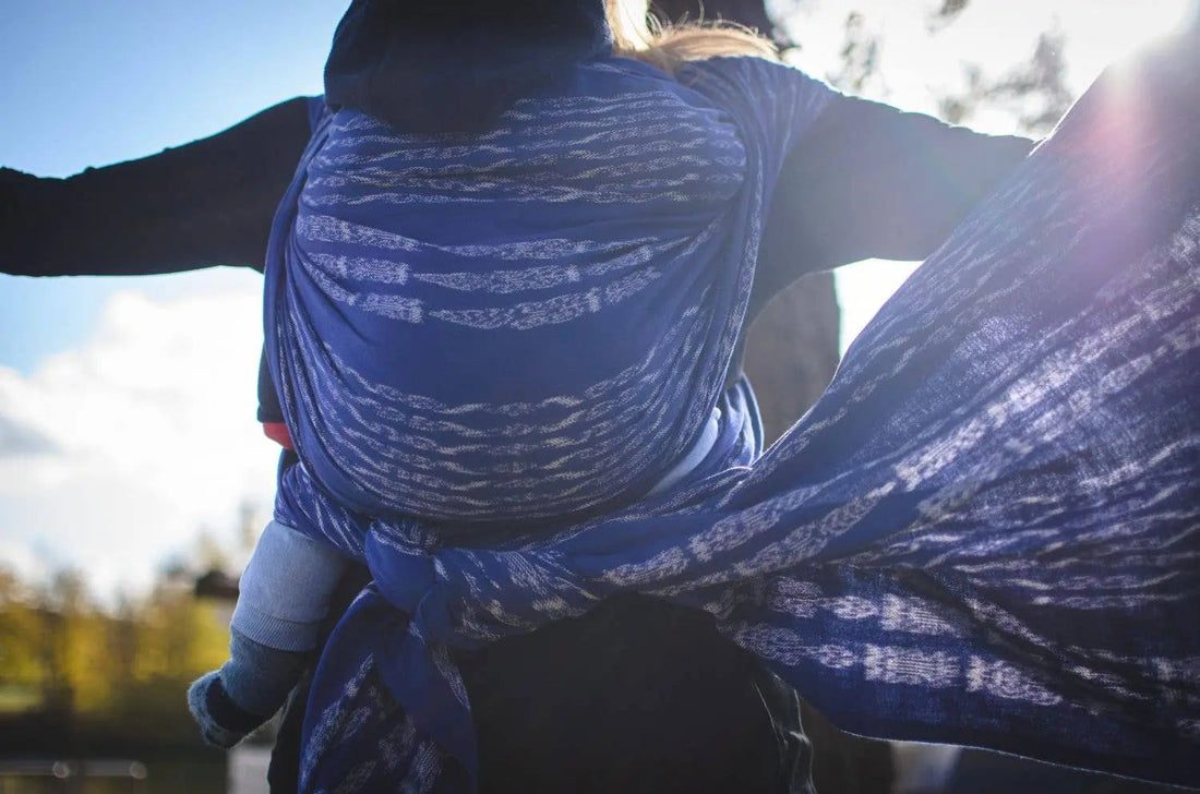 A person back carrying their infant outside in a purple and blue woven wrap by Girasol