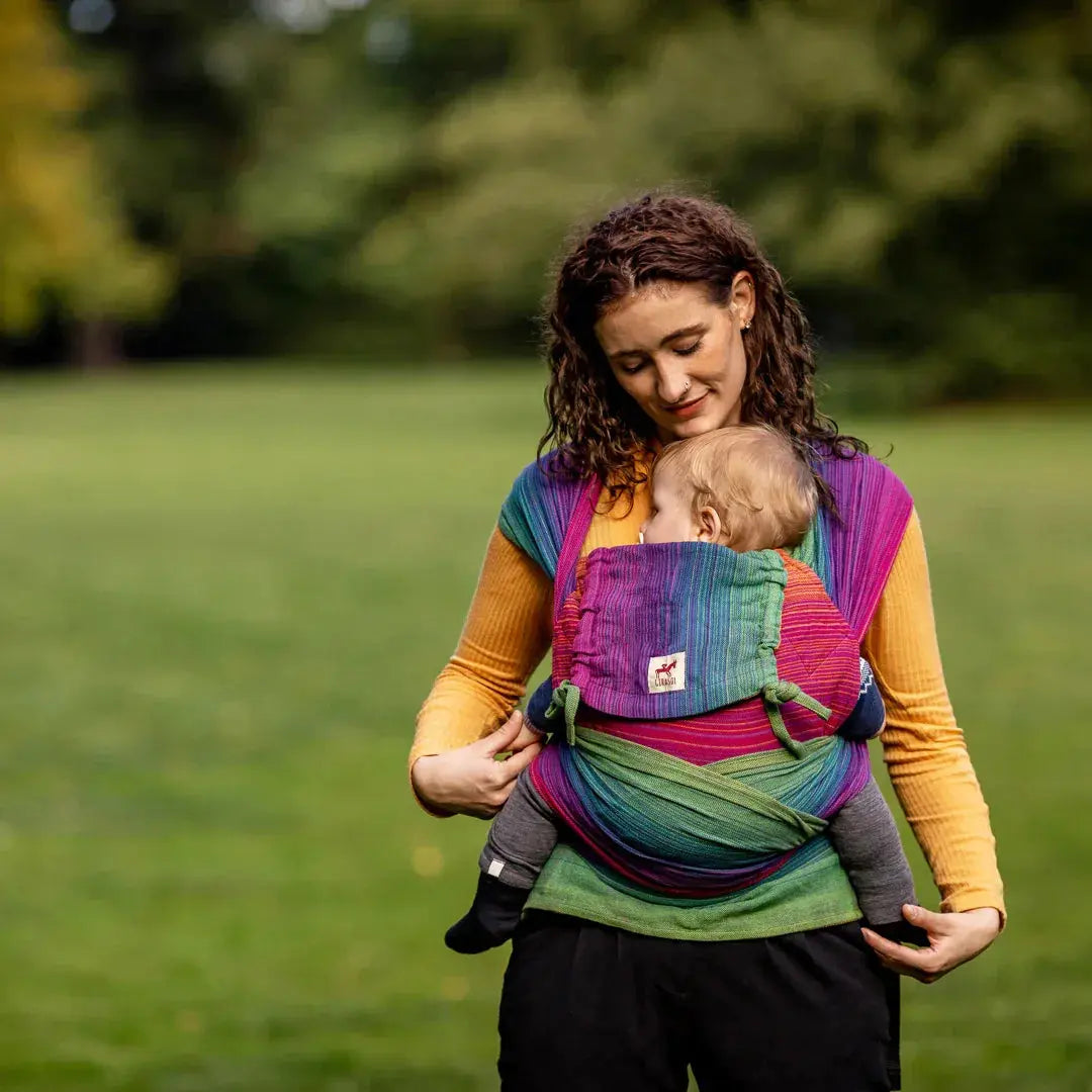 A mother babywearing her infant in a Paradise WrapMySol Mei Tai outside in an open field